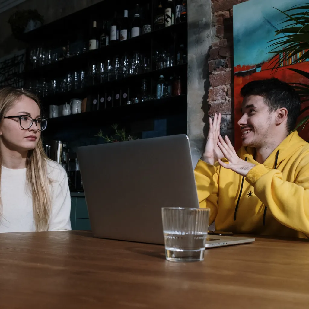 A man in a yellow hoodie grins as he signs to a woman in glasses across a café table, and she follows along. He's telling a good story. The people at the next table will never know how it ends.